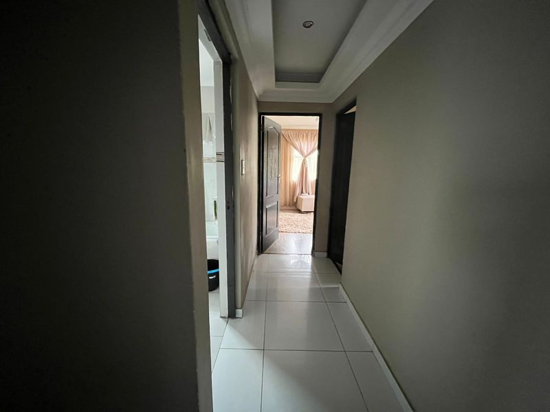 A clean, tiled hallway featuring a recessed ceiling design with integrated downlighting, providing access to adjacent rooms.