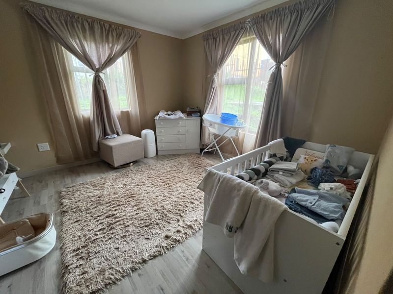 A bedroom featuring laminate flooring and dual windows with curtain rails, providing natural light and a neutral color palette.