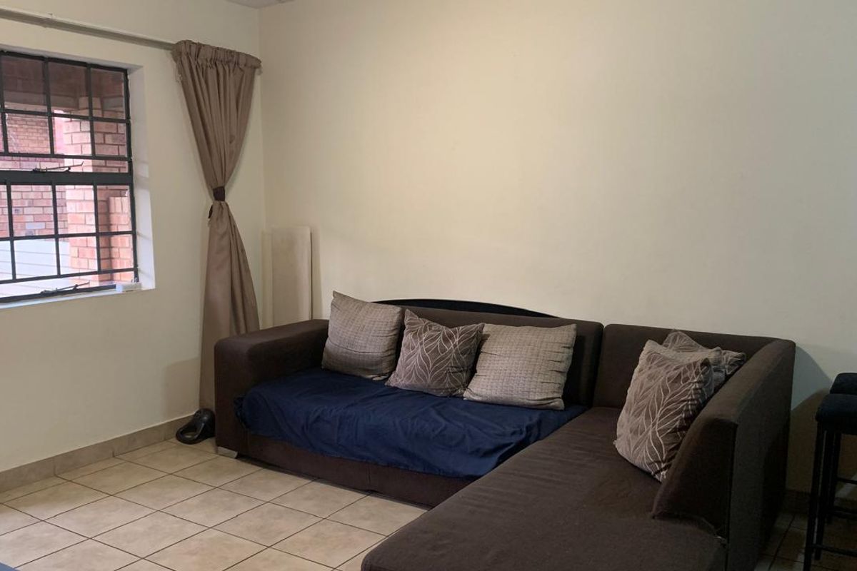 A living room area featuring neutral tiled flooring and a window fitted with security bars.