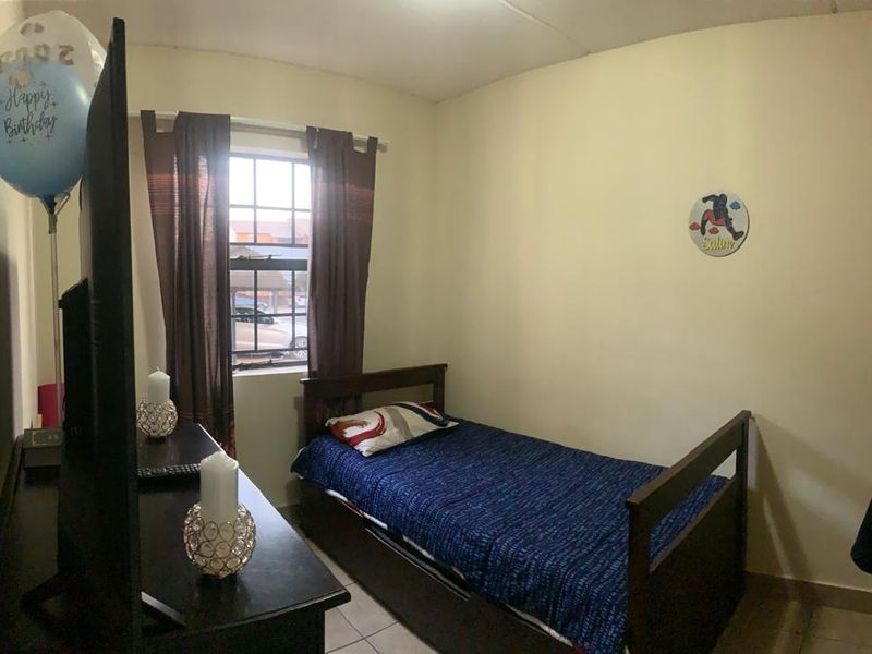 A compact bedroom featuring tiled flooring, a built-in wardrobe, and a window with security bars, providing a functional living space.