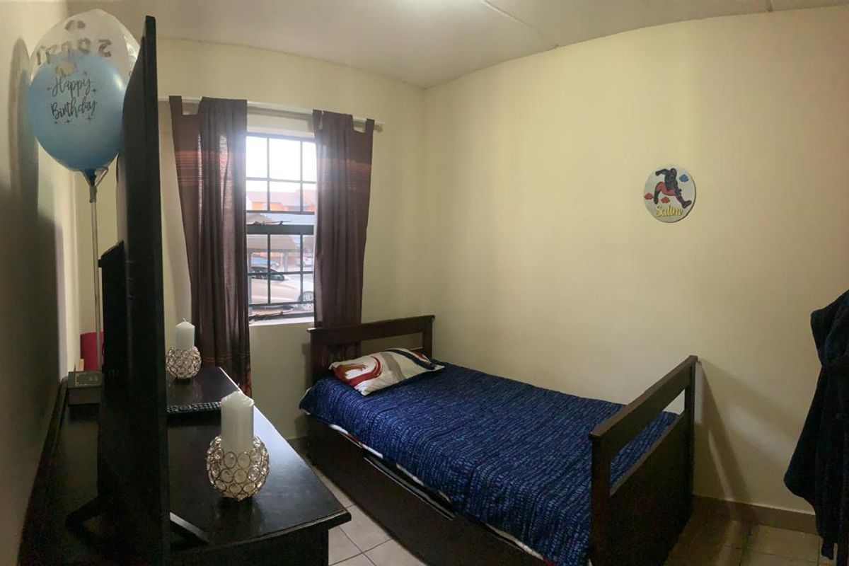 A compact bedroom featuring tiled flooring, a built-in wardrobe, and a window with security bars, providing a functional living space.