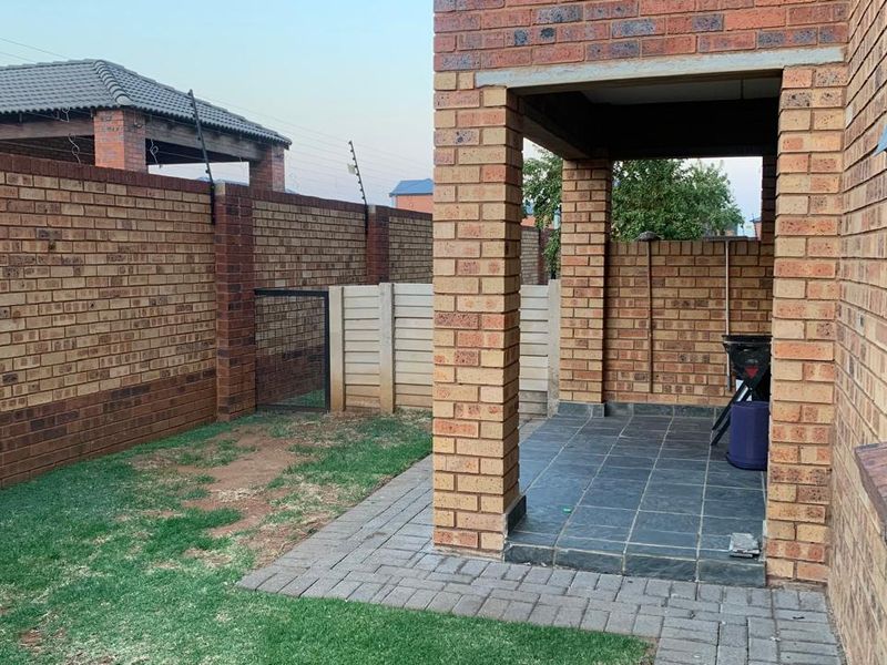 A rear exterior view featuring a covered brick patio with tiled flooring, adjacent to a small garden area enclosed by brick boundary walls.