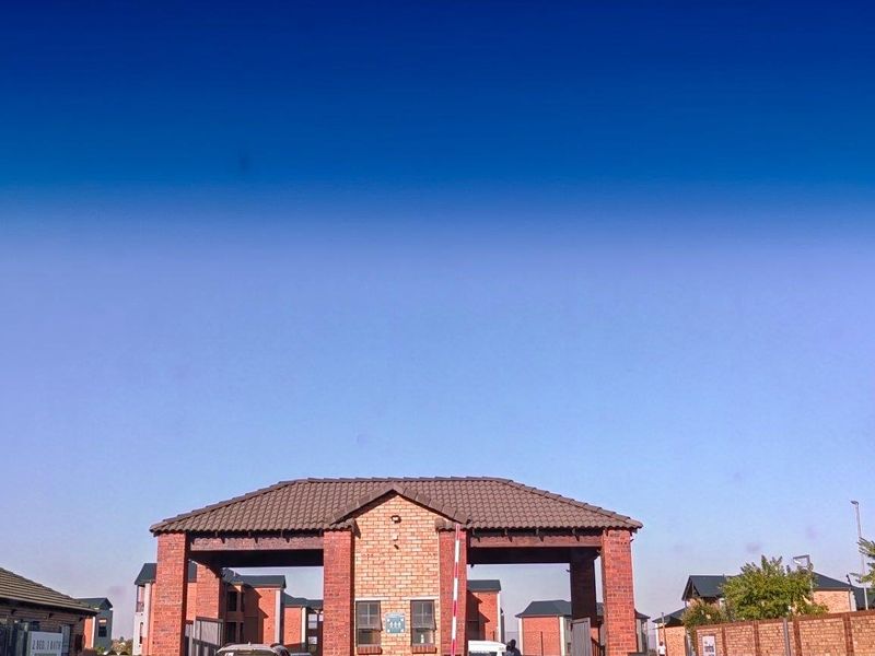 View of the apartment complex entrance featuring a brick security gatehouse and perimeter walling under a clear sky.