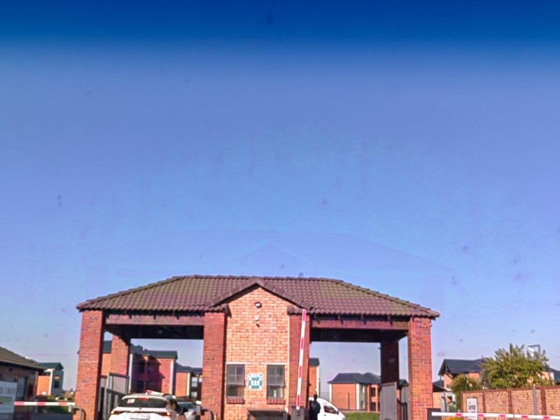 The entrance to the apartment complex features a brick security gatehouse with a tiled roof and controlled access boom gates.