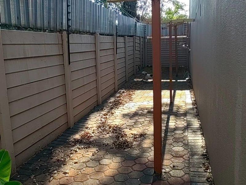 A narrow side passage featuring paved flooring, a precast concrete boundary wall with electric fencing, and a fixed metal washing line structure.