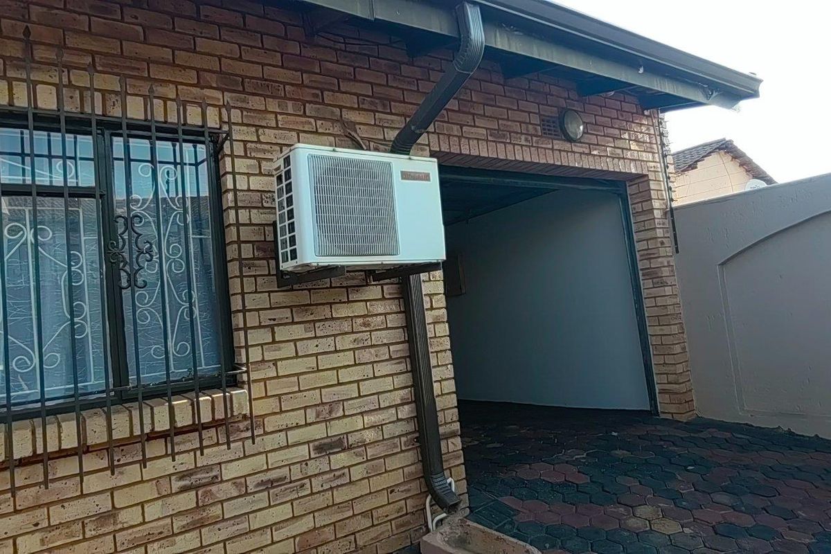 Exterior view of a face brick property featuring security bars on the window, an external air conditioning unit, and paved driveway area.