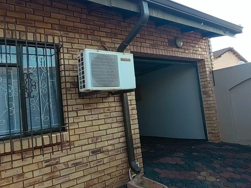 Exterior view of a face brick property featuring security bars on the window, an external air conditioning unit, and paved driveway area.