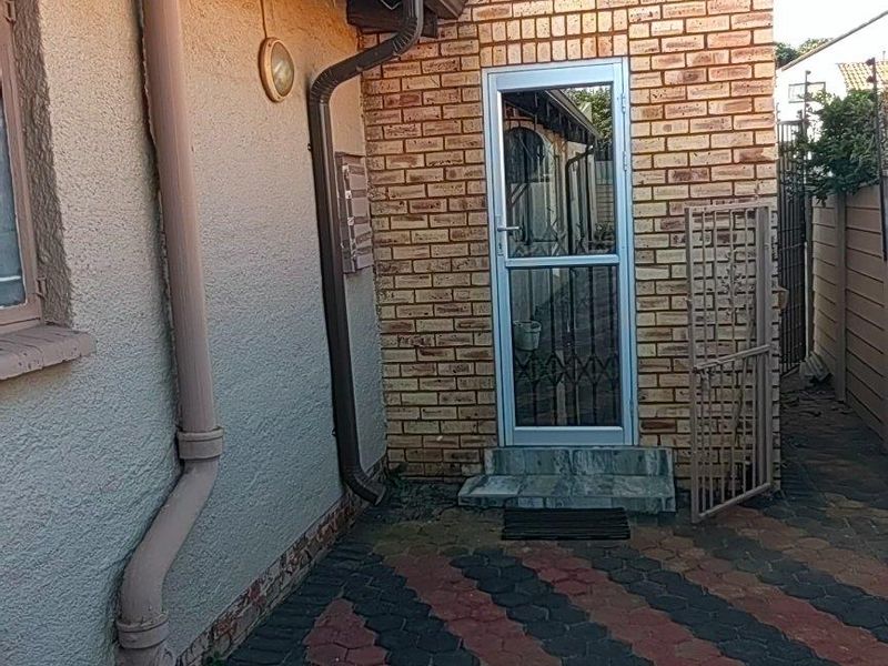 Rear exterior view of the property featuring brick wall construction, paved ground surface, and a secure metal entrance door.