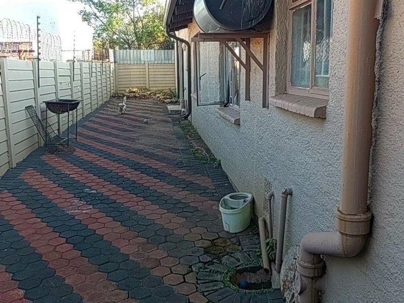 Side exterior view of the property featuring a paved walkway, solar water heater installation, and perimeter precast concrete walling.