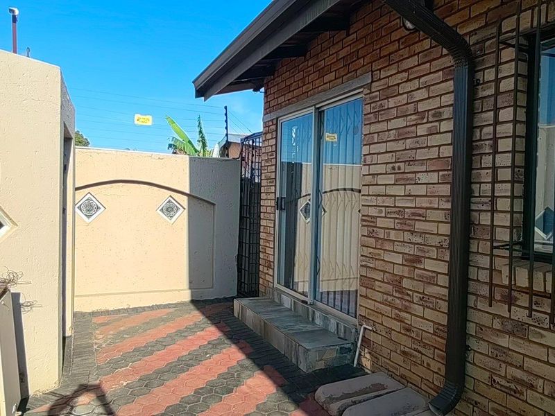 A private rear courtyard featuring face brick exterior, paved flooring, and a sliding glass door with security bars.