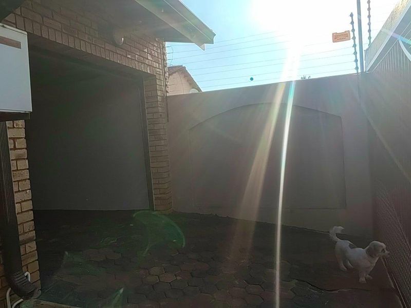 Exterior view of a garage area featuring brick construction, paved driveway, and perimeter security fencing.