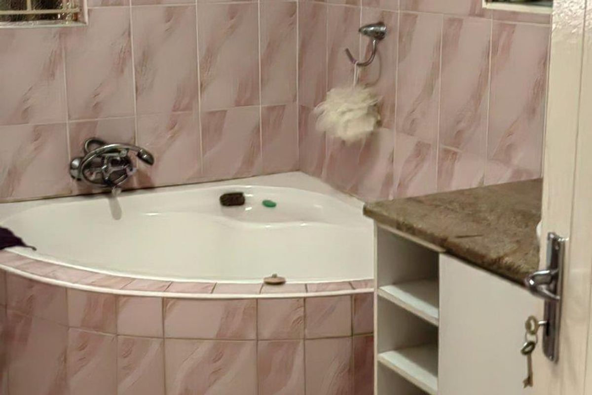 Bathroom featuring a corner bathtub, tiled finishes, and a vanity cabinet with stone countertop and built-in shelving.
