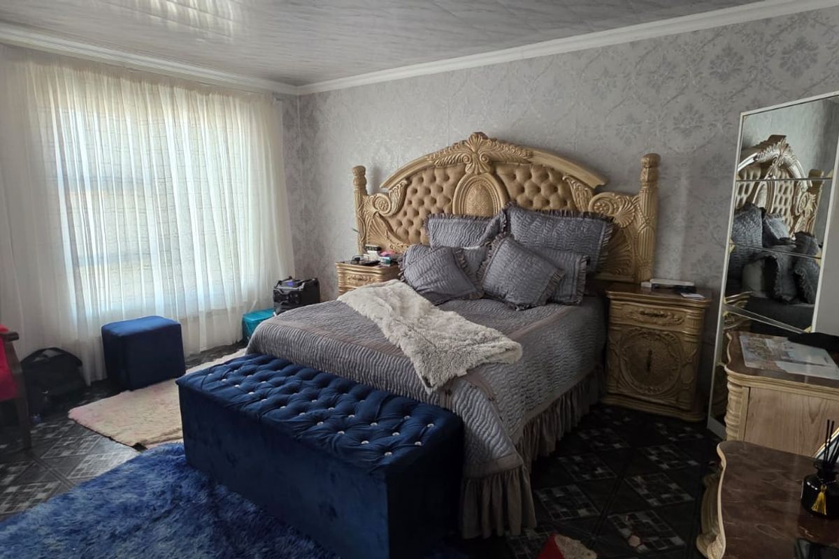 A spacious bedroom featuring patterned wallpaper, tiled flooring, and large windows with sheer curtains.