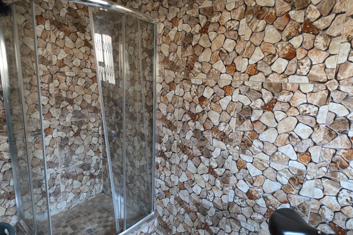 A bathroom featuring a glass-enclosed shower stall with distinctive stone-patterned wall tiling throughout the space.