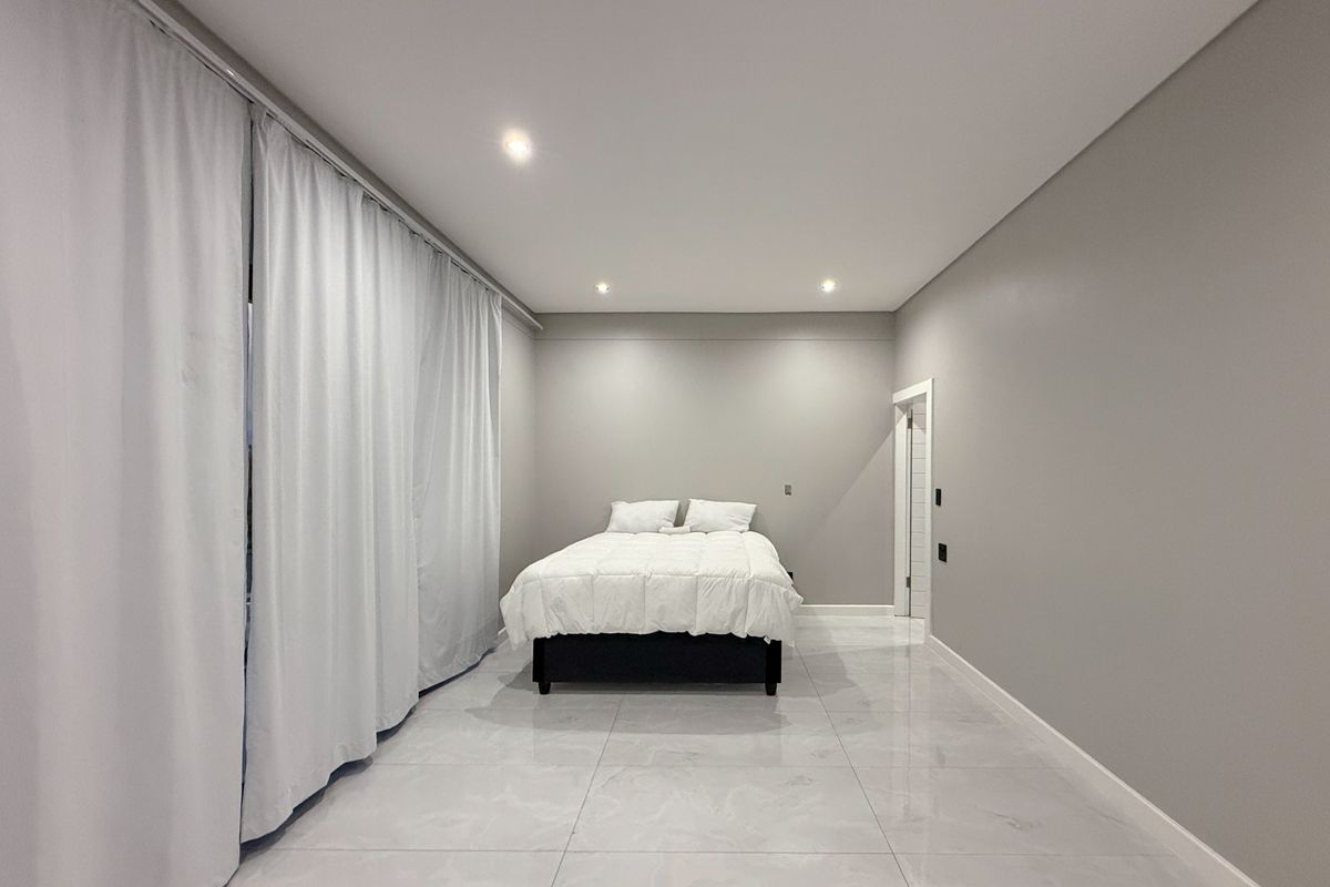 A spacious, modern bedroom featuring polished marble-style floor tiles, recessed ceiling lighting, and neutral grey walls.