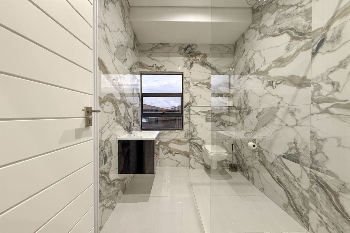Modern bathroom featuring floor-to-ceiling marble-look tiling, a wall-mounted vanity, a frameless glass shower enclosure, and a wall-hung toilet.