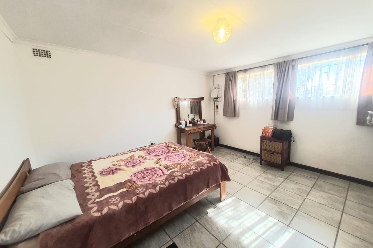 A functional bedroom featuring tiled flooring, built-in ventilation, and large windows allowing for natural light.