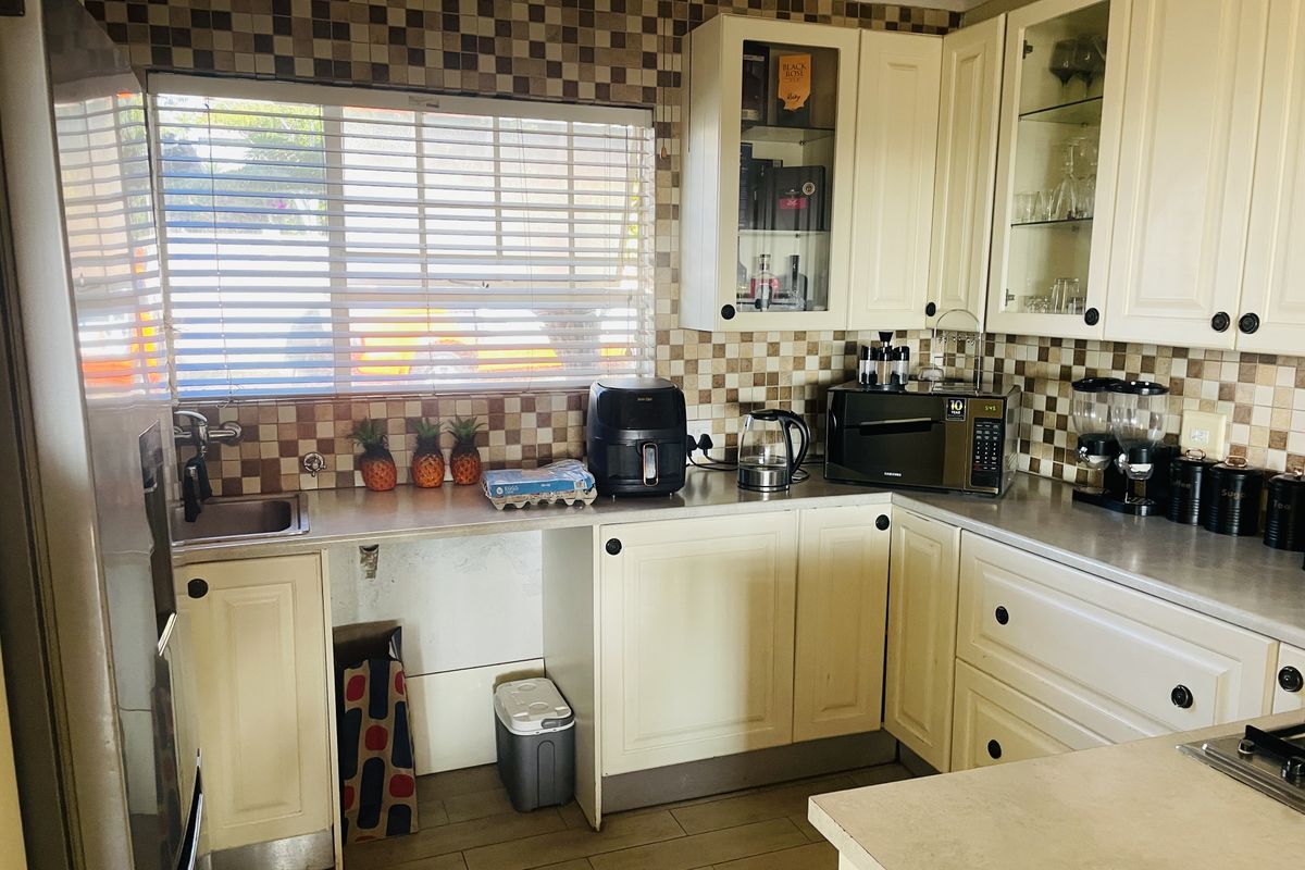A functional kitchen featuring cream-colored cabinetry, a tiled backsplash, and a stainless steel sink, offering a practical layout for daily meal preparation.