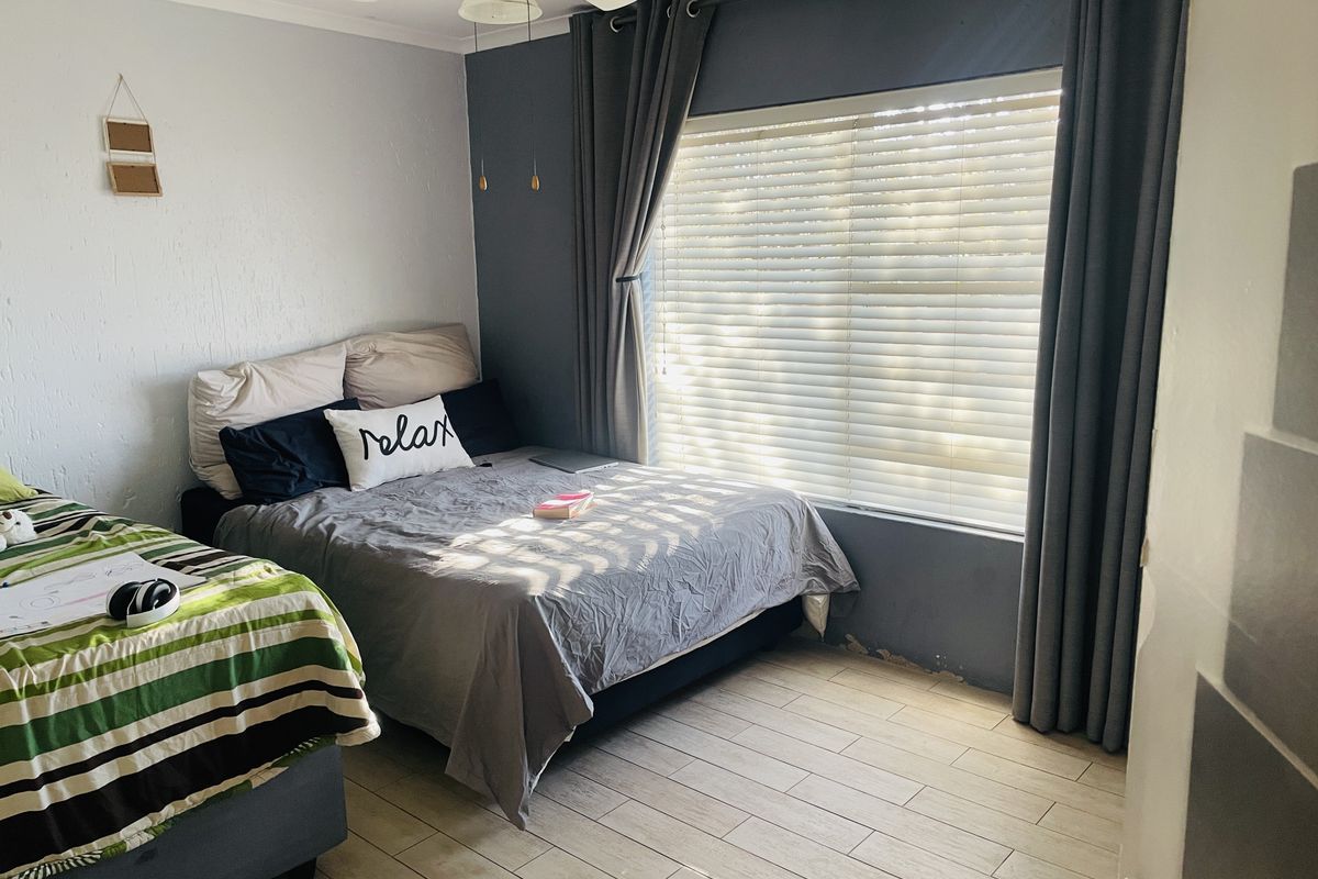 A bedroom featuring tiled flooring, a ceiling fan, and a large window with blinds, providing natural light.