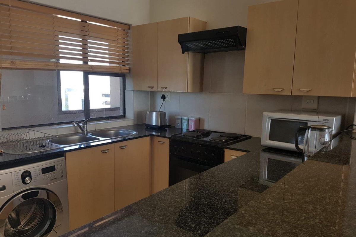 A functional kitchen featuring granite countertops, built-in cabinetry, an electric hob with extractor fan, and a double sink with integrated laundry plumbing.