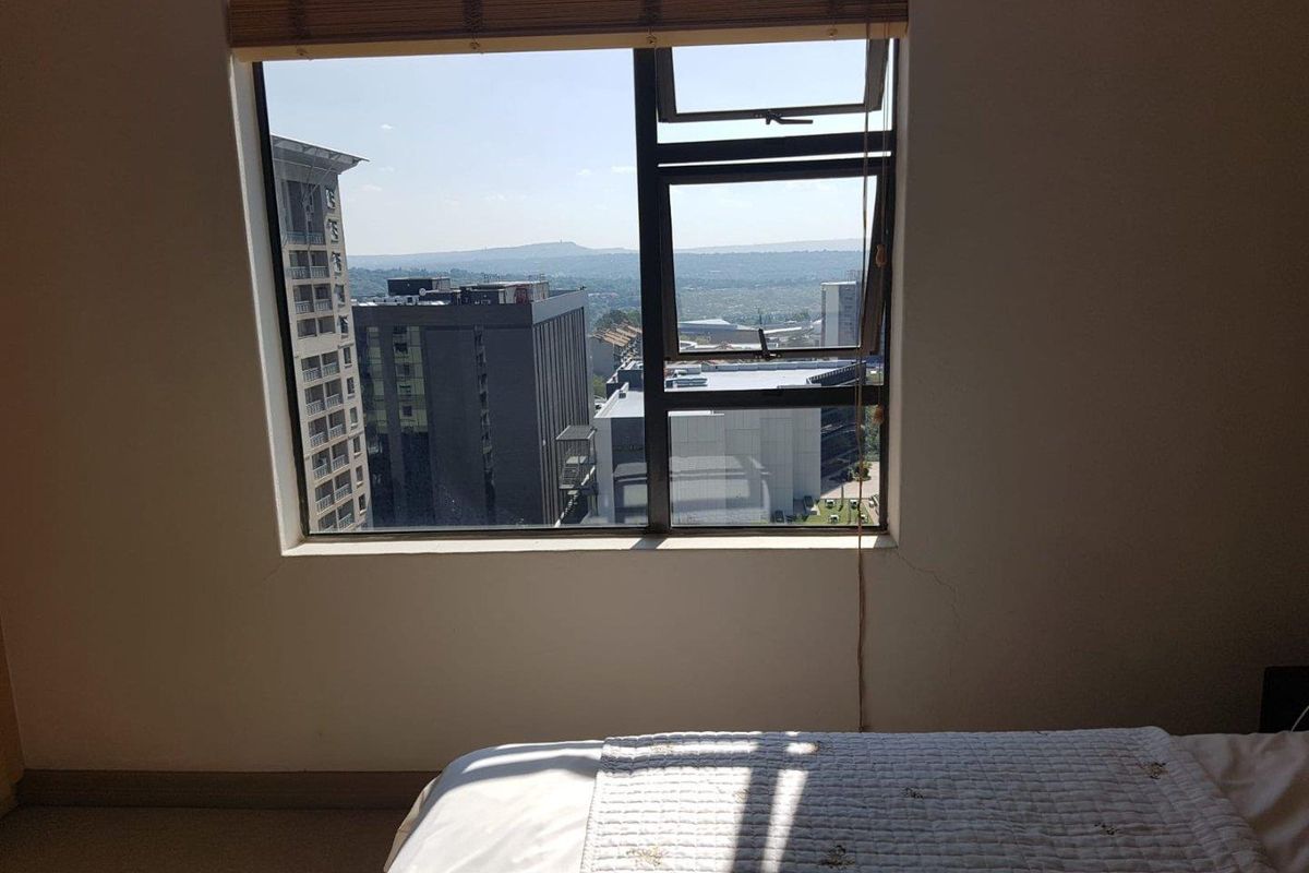 Bedroom featuring a large window with an urban city view and a fitted bamboo blind.