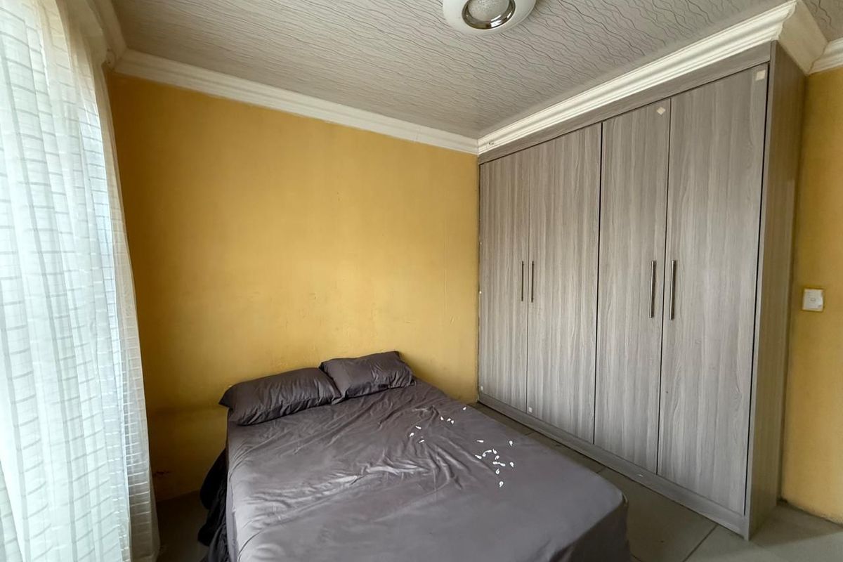 A bedroom featuring built-in wooden wardrobes, tiled flooring, and a textured ceiling finish.