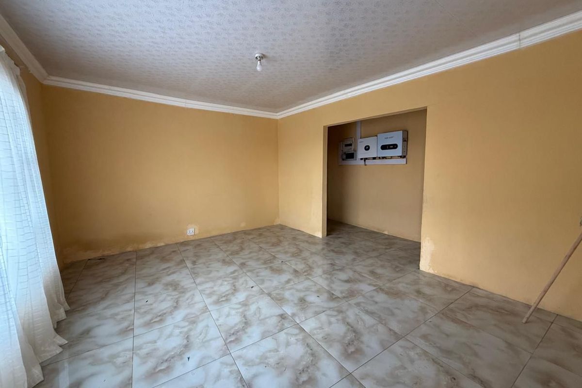An empty living room featuring tiled flooring, crown molding, and a recessed alcove housing an inverter and electrical distribution board.