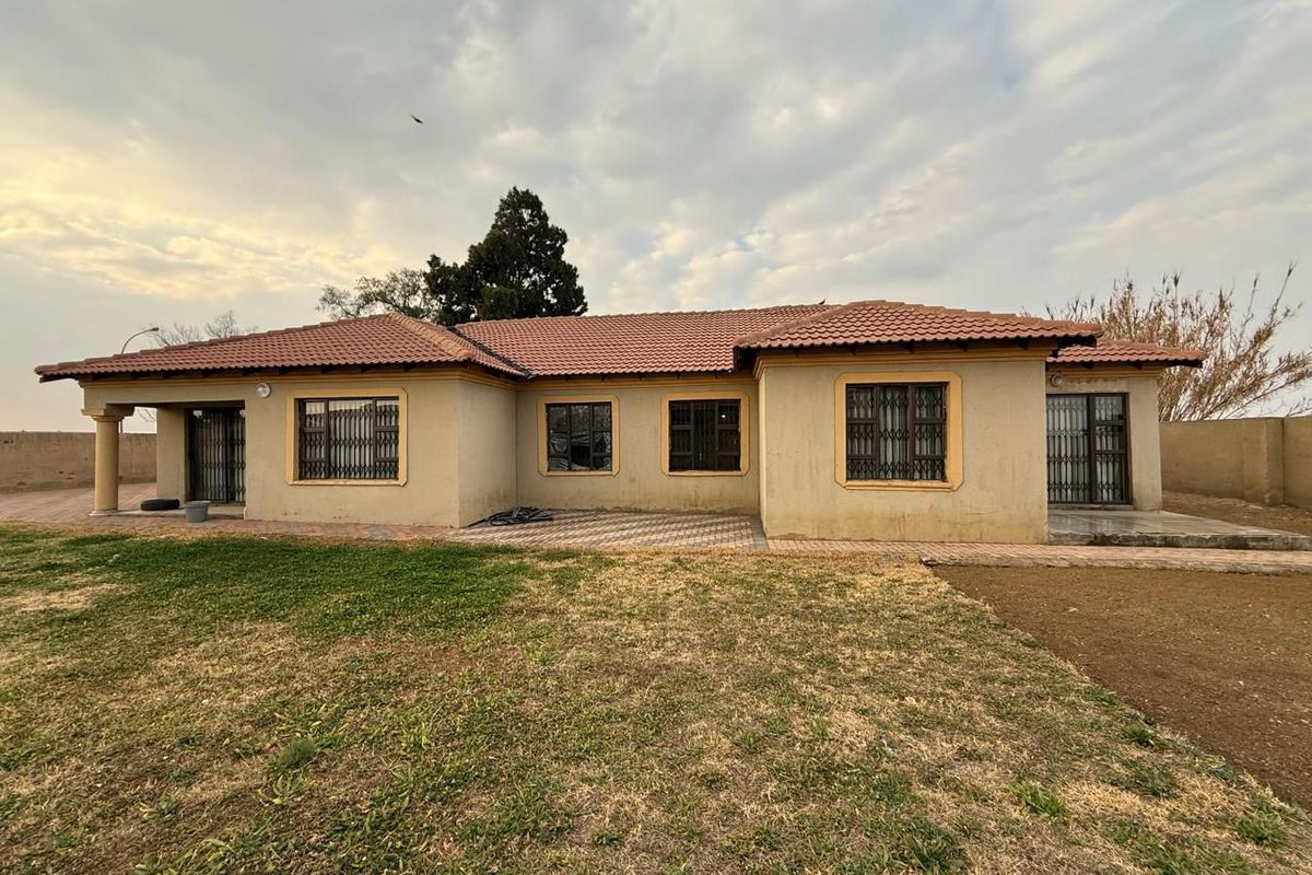 A single-story residential property featuring a tiled roof, paved patio area, and security gates on windows and doors, set on a spacious plot.
