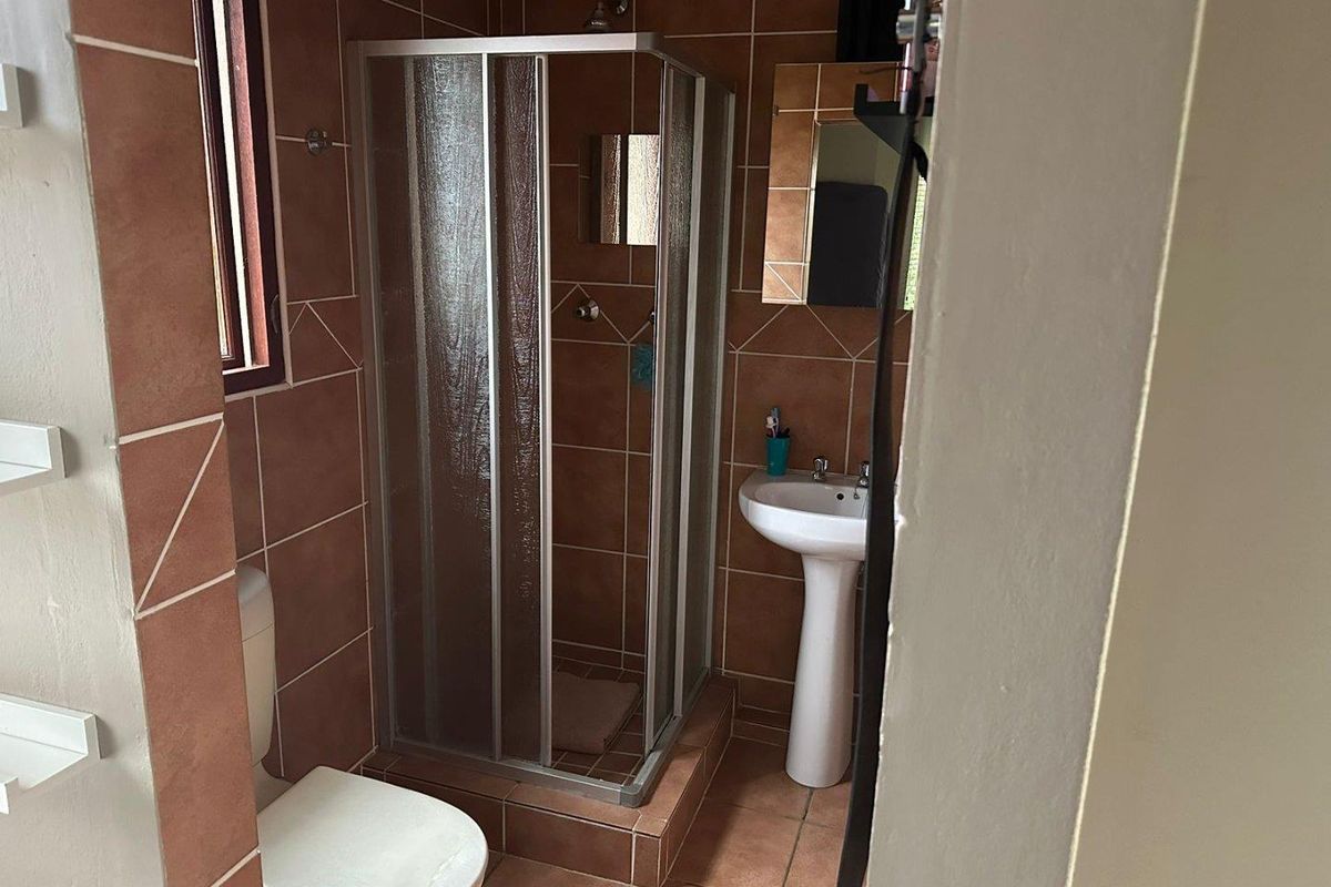 A compact bathroom featuring a shower enclosure, pedestal basin, and toilet, finished with terracotta-toned wall and floor tiles.