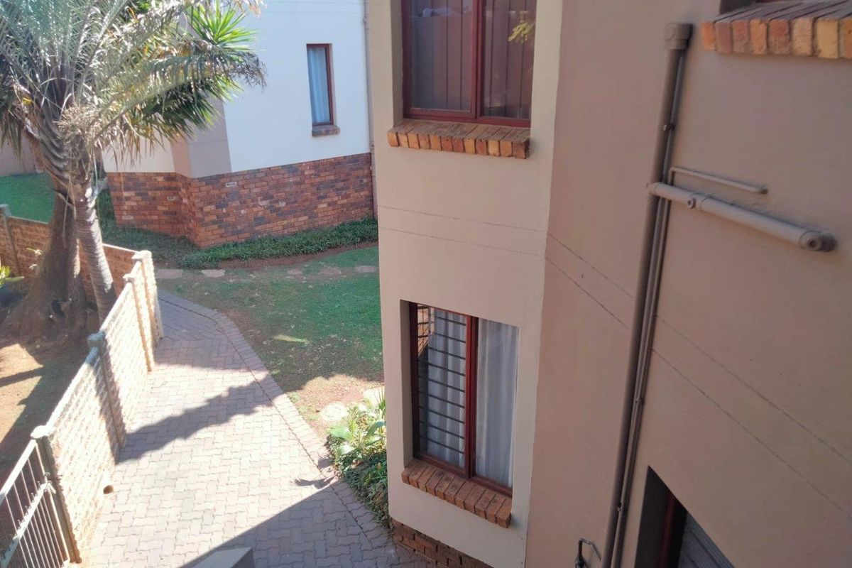 An elevated view of the apartment complex rear exterior, featuring brick paved pathways, landscaped garden areas, and secure window fixtures.