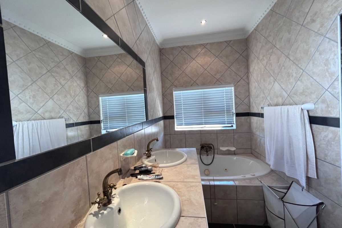 A bathroom featuring a double vanity with drop-in sinks, a built-in corner bathtub, and tiled walls with a decorative border.