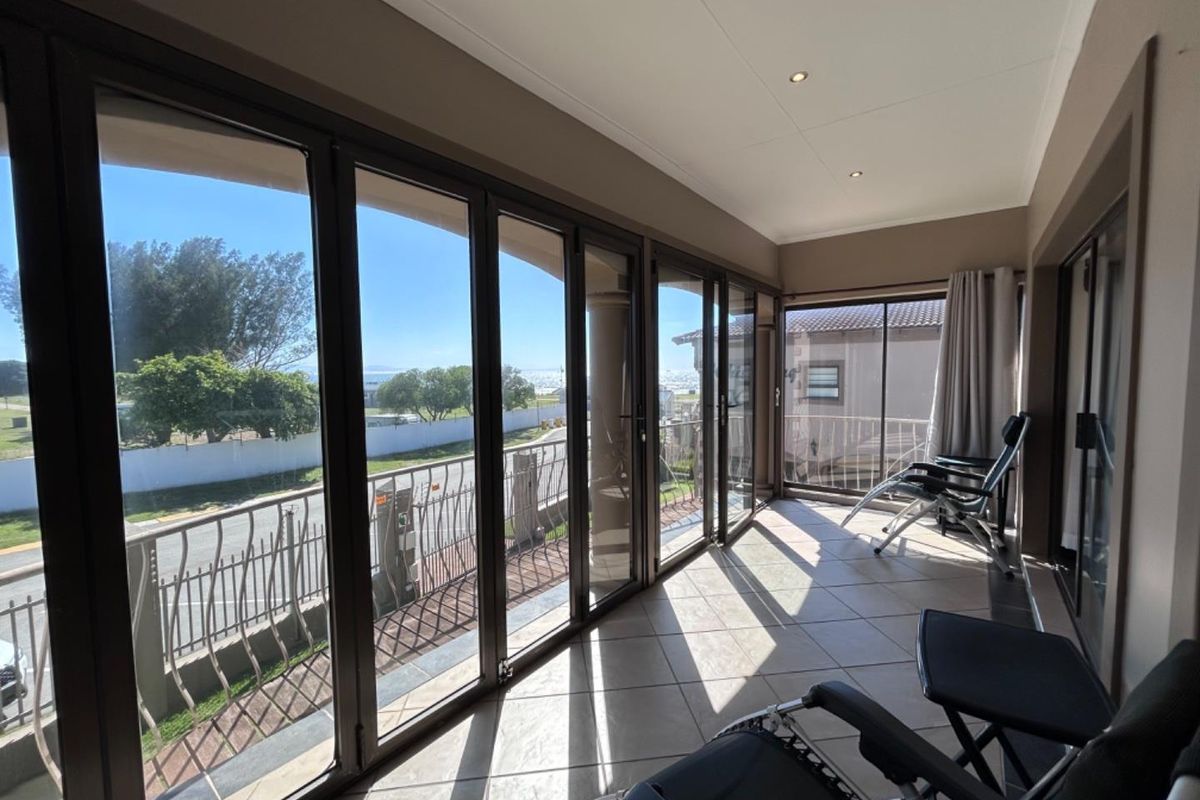 A bright, enclosed patio featuring large floor-to-ceiling folding glass doors, tiled flooring, and recessed ceiling lighting, offering an expansive view of the surroundings.