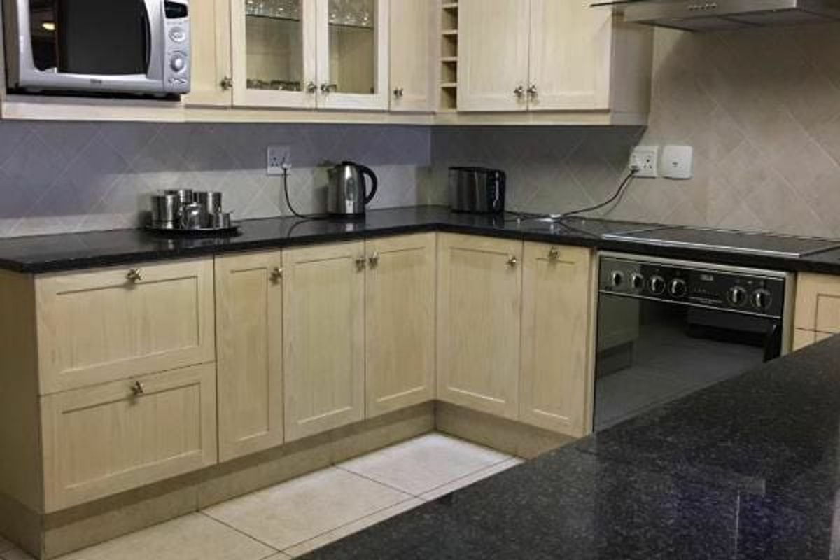 A functional kitchen featuring light wood cabinetry, dark granite countertops, tiled backsplash, and a built-in oven with an extractor fan.