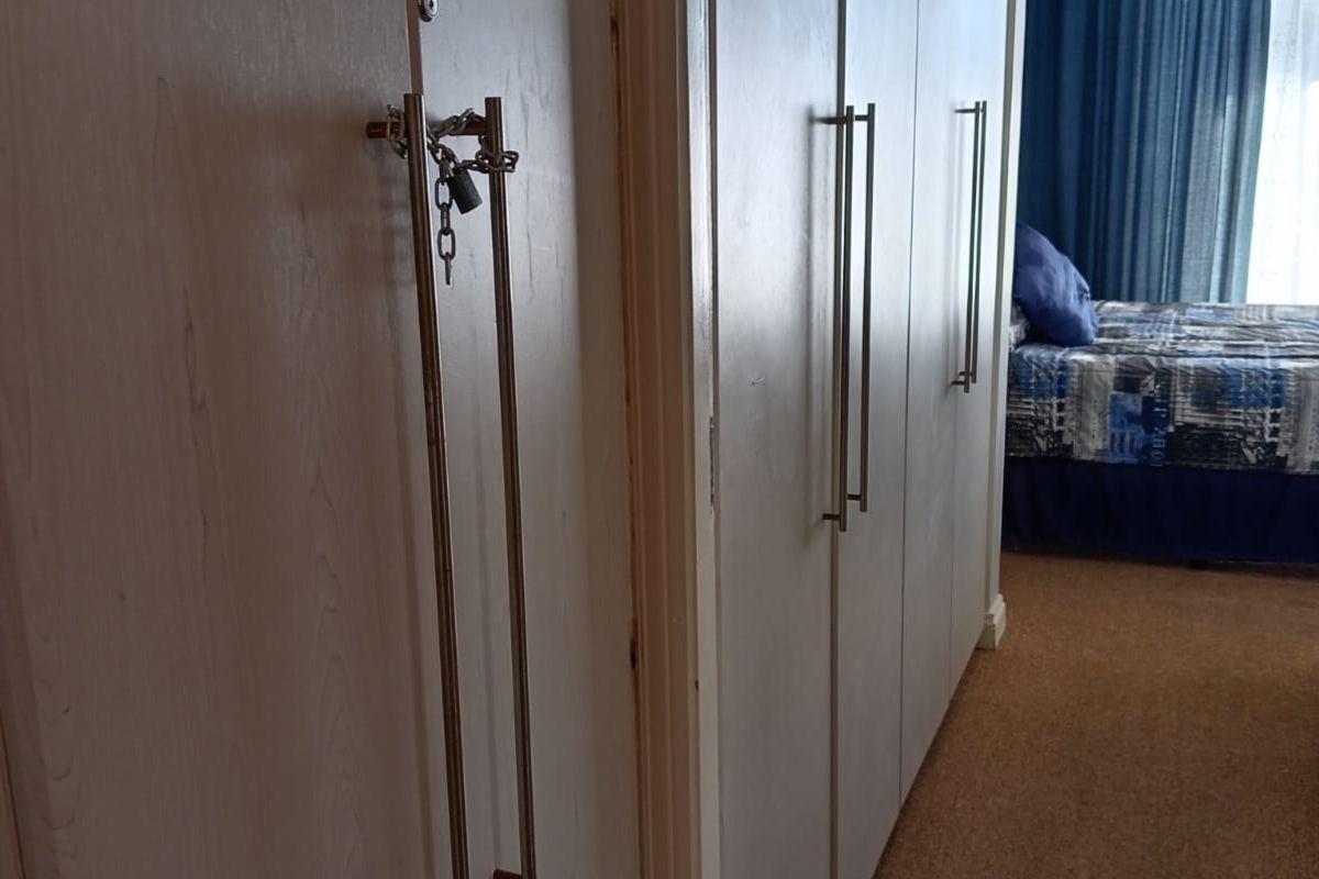 A bedroom featuring extensive built-in floor-to-ceiling cabinetry with modern handles and carpeted flooring, leading into a sleeping area with natural light.