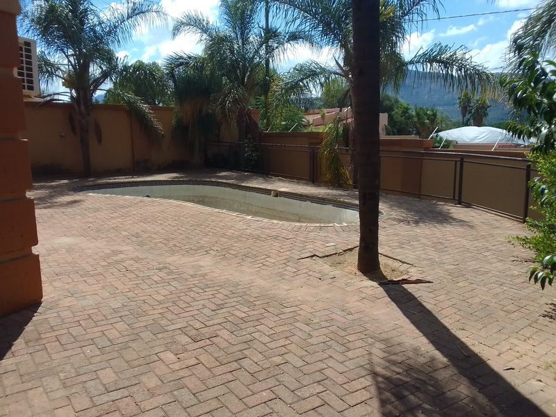 Outdoor pool area featuring brick paving, boundary walls, and an empty swimming pool requiring maintenance.