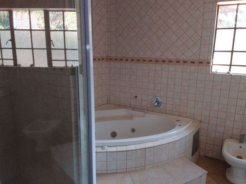 A functional bathroom featuring a corner spa bath, bidet, and a glass-enclosed shower with neutral wall tiling.