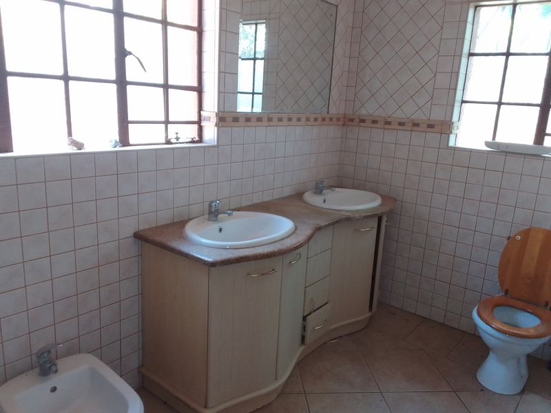 A dated bathroom featuring a double vanity with dual basins, a bidet, a toilet, and tiled finishes throughout, requiring cosmetic updates.