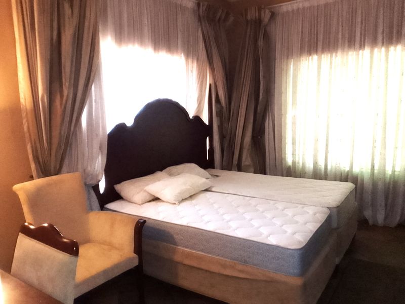 A bedroom featuring large windows with layered curtains, providing natural light. The space is furnished with a bed and an armchair.