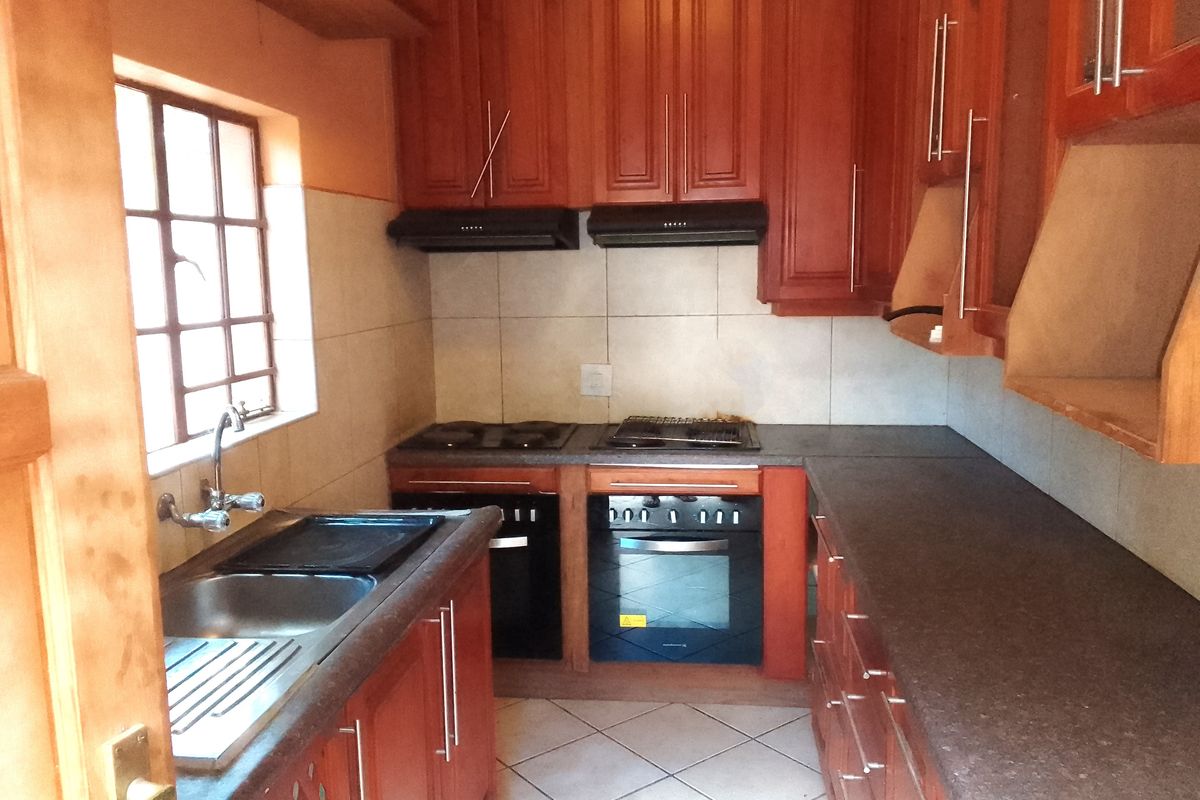 A functional kitchen featuring wooden cabinetry, built-in oven, electric hob, extractor fan, and tiled finishes, offering a practical layout for meal preparation.