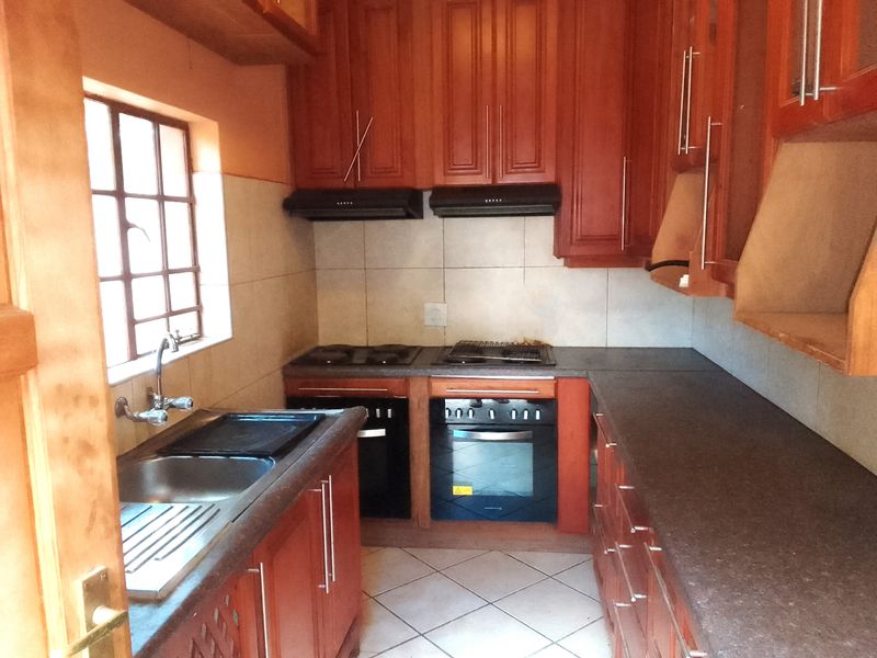 A functional kitchen featuring wooden cabinetry, built-in oven, electric hob, extractor fan, and tiled finishes, offering a practical layout for meal preparation.