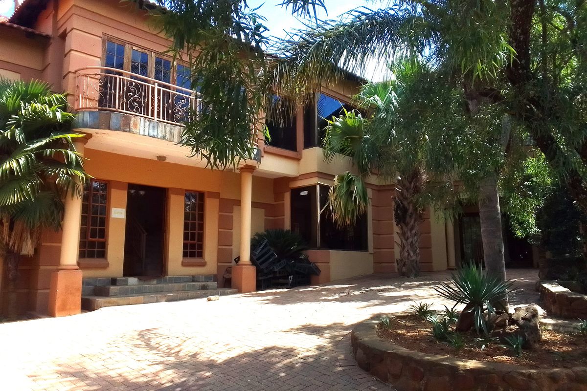 Rear exterior view of a multi-story guest house featuring a paved courtyard, stone-clad garden beds, and a second-floor balcony with wrought iron railings.
