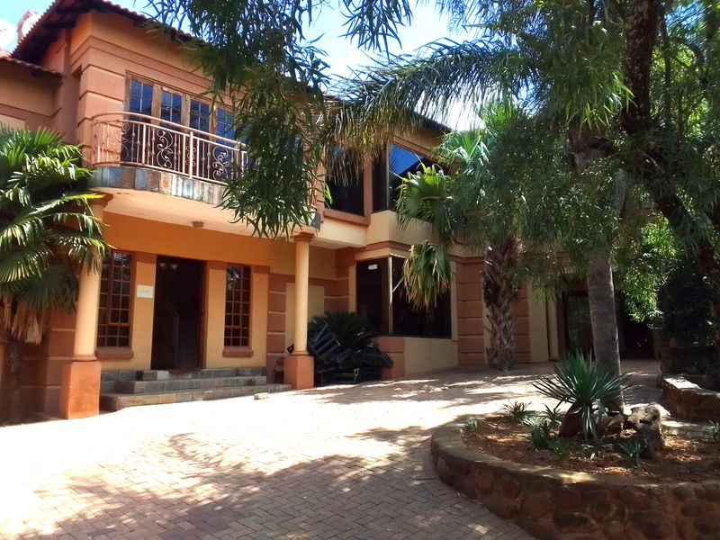 Rear exterior view of a multi-story guest house featuring a paved courtyard, stone-clad garden beds, and a second-floor balcony with wrought iron railings.
