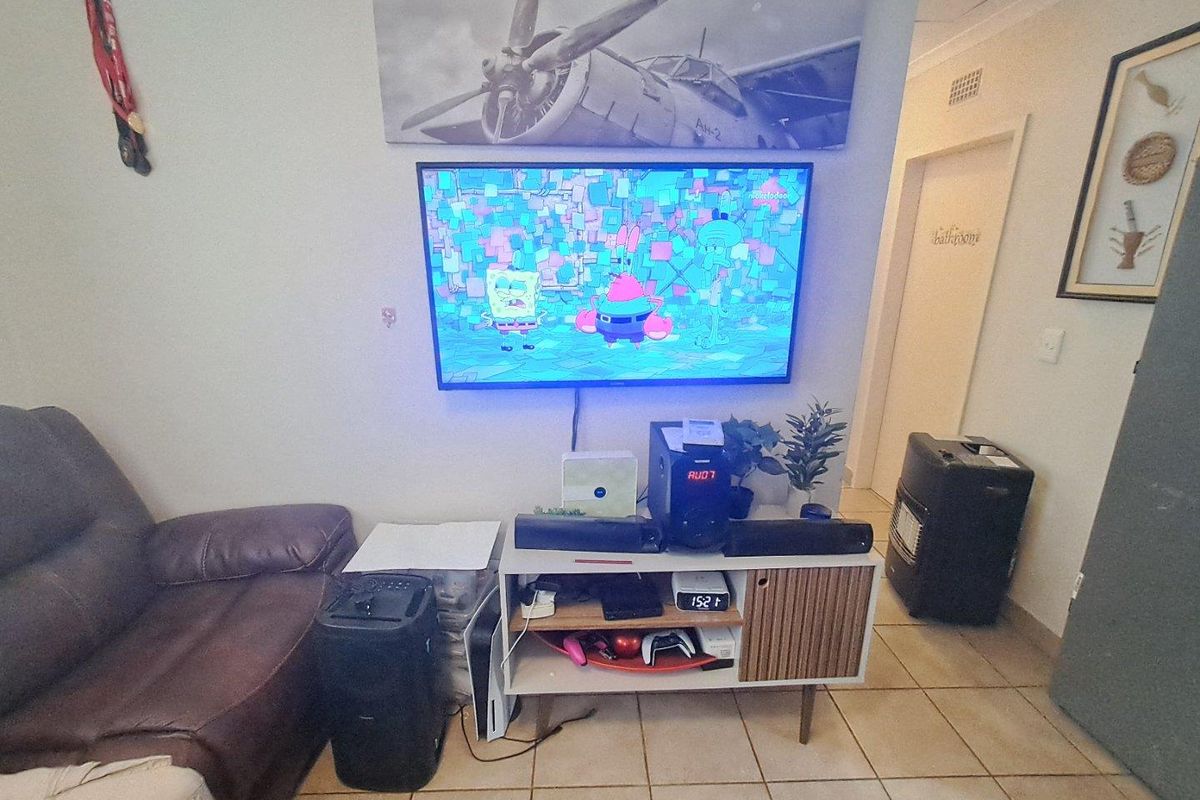A living room area featuring tiled flooring and a wall-mounted television setup.