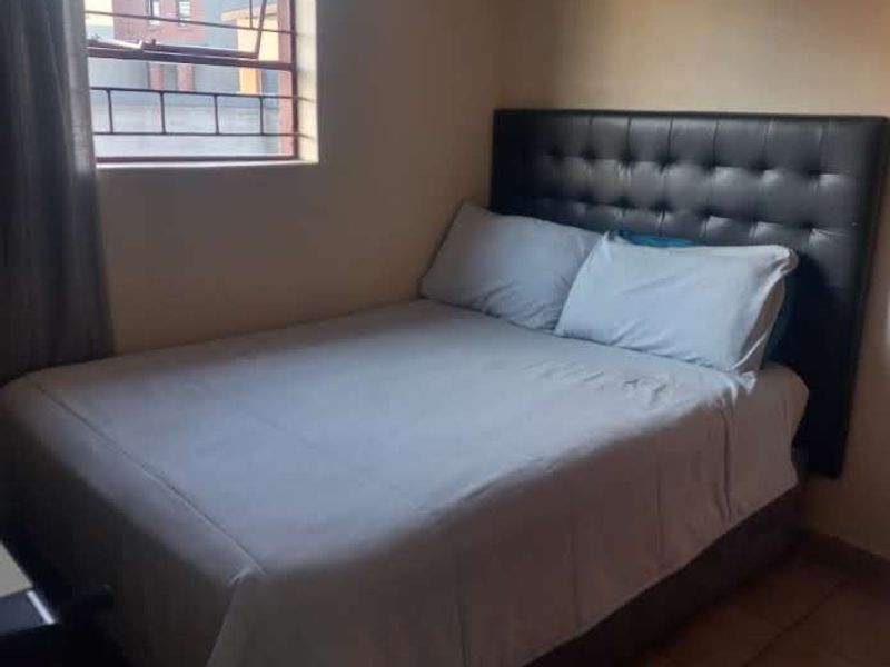 A functional bedroom featuring tiled flooring and a window fitted with security burglar bars.
