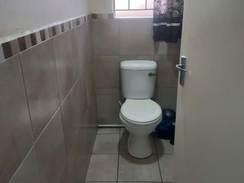 A compact guest bathroom featuring neutral wall and floor tiling, a standard toilet, and a window with security bars.