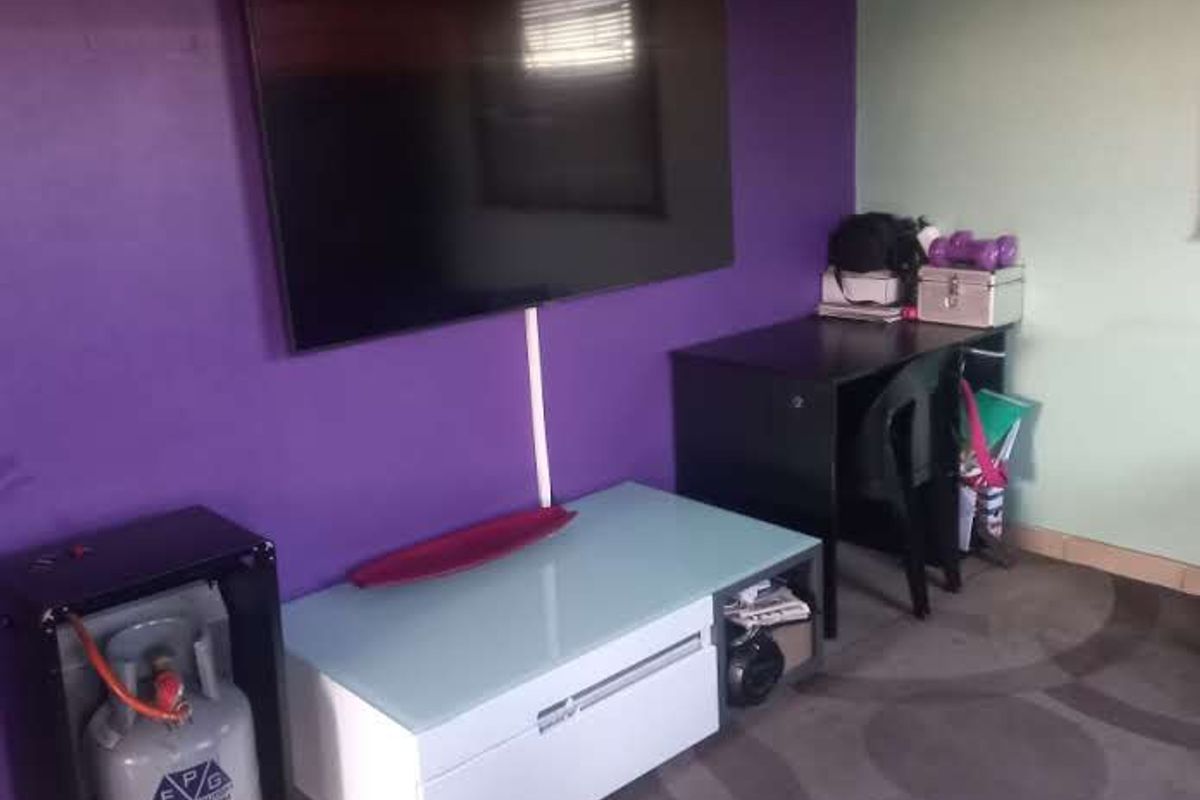 A living area featuring tiled flooring and a wall-mounted television, currently used as a multi-purpose space.