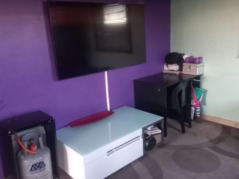A living area featuring tiled flooring and a wall-mounted television, currently used as a multi-purpose space.