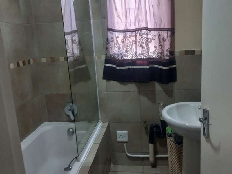 A functional bathroom featuring a bathtub with a glass screen, tiled finishes, and a pedestal basin.