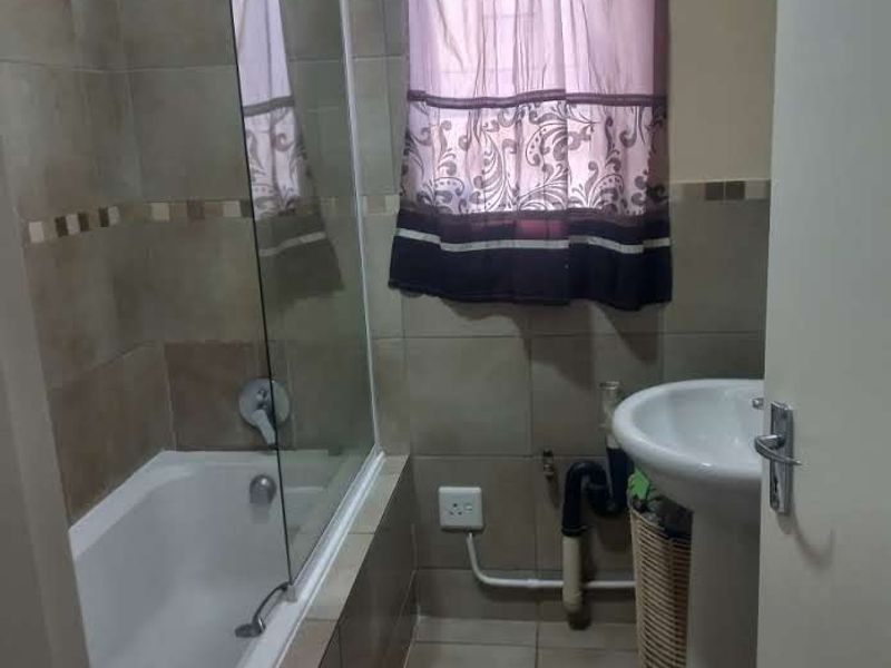 A functional bathroom featuring a bathtub with a glass screen, tiled finishes, and a pedestal basin with exposed plumbing.