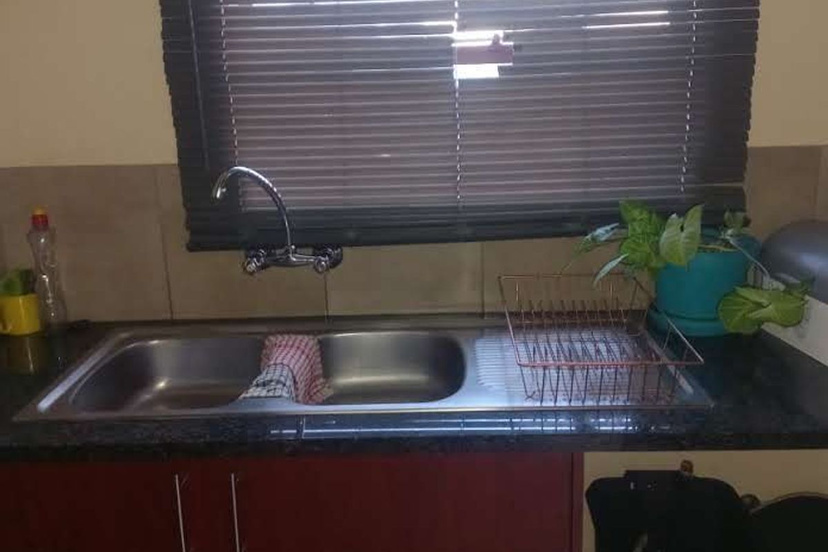 A functional kitchen sink area featuring a double bowl stainless steel sink, granite countertop, and dark wood-look cabinetry with venetian blinds.